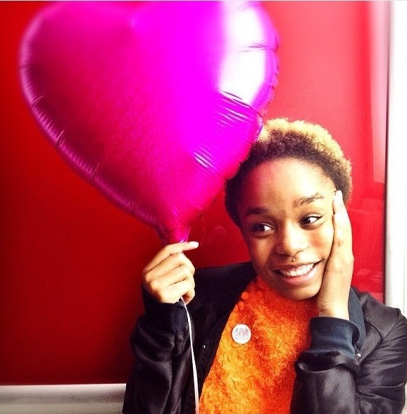 Afi Baaqi smiling while holding a bright pink heart-shaped balloon